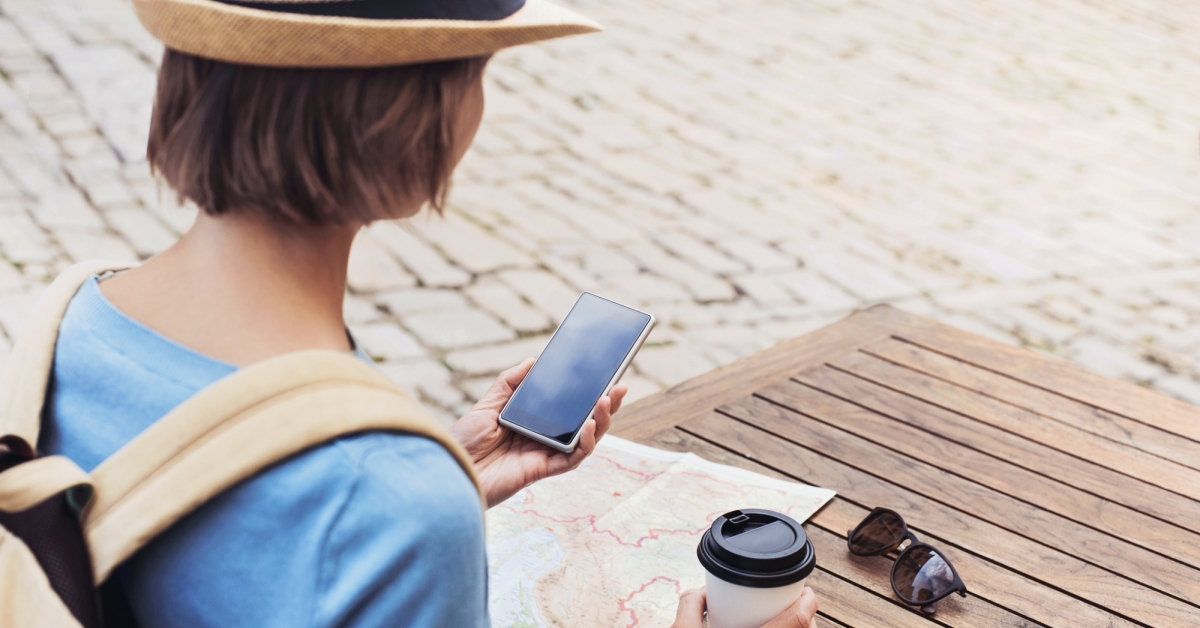 Young woman with map and coffee cup holds mobile 