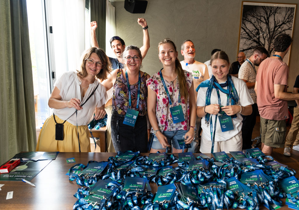 Attendees smiling and cheering at the registration desk, with badges and lanyards spread across the table